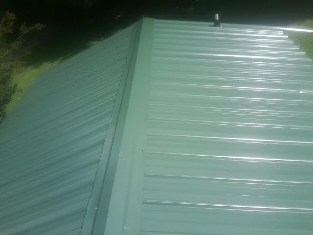 New green metal panels meeting at the ridge of a roof — Flat Roof Repair work by our crew in Grandview